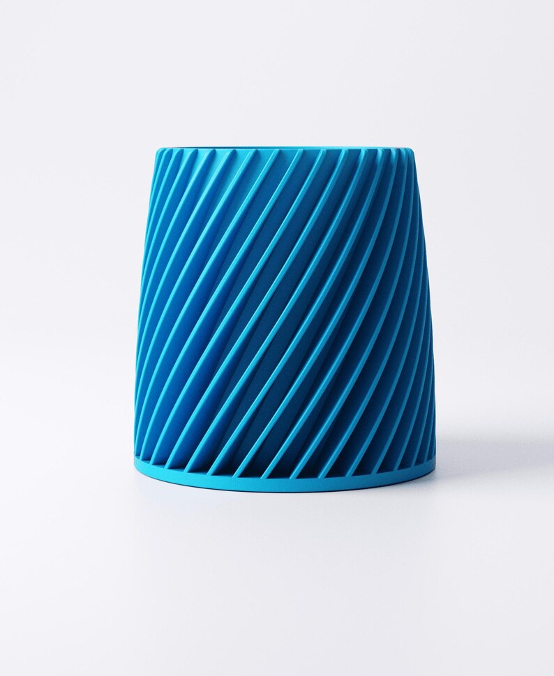 K&ouml;nnte beinhalten: Ein leuchtend blauer zylindrischer Beh&auml;lter mit einem spiralf&ouml;rmigen Rippendesign. Der Beh&auml;lter hat einen festen Boden und eine leicht ausgestellte Oberseite. Die diagonalen Linien erzeugen einen dynamischen visuellen Effekt. Der Gegenstand steht vor einem schlichten wei&szlig;en Hintergrund.