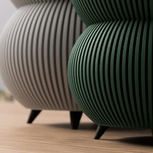 May include: Two decorative, modern accent tables. One is a light gray color, and the other is a dark green. Both have a ribbed design and sit on three black legs. The tables are on a light brown wooden floor.