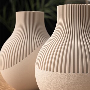 May include: Two beige decorative vases with a textured, ribbed design. The vases have a rounded shape with a textured base and a ribbed, vertical pattern on the upper portion. The vases are likely used for home decor.