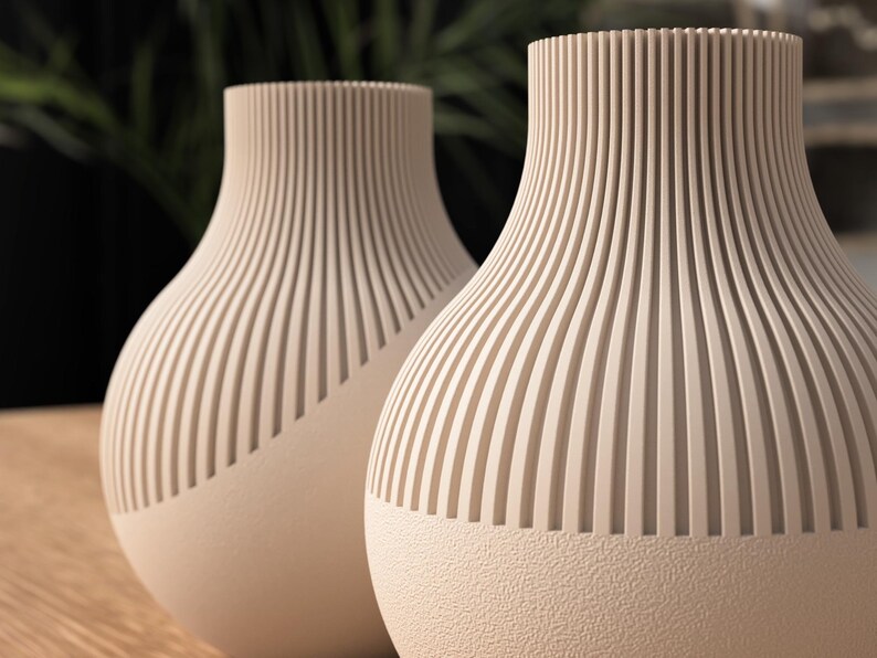May include: Two beige decorative vases with a textured, ribbed design. The vases have a rounded shape with a textured base and a ribbed, vertical pattern on the upper portion. The vases are likely used for home decor.