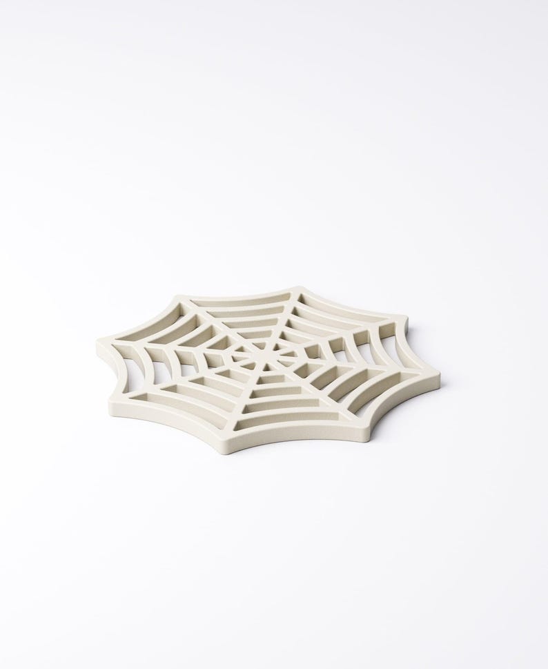 May include: A light beige, spider web-shaped trivet. The trivet is made of a solid material and features a detailed web design. The trivet is designed to protect surfaces from hot items. A decorative item for the kitchen.