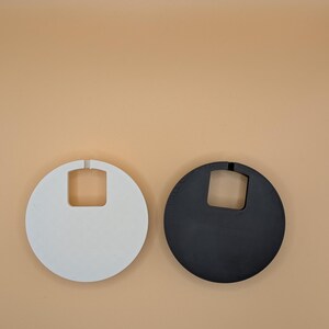 K&ouml;nnte beinhalten: Zwei runde Handtaschen, eine wei&szlig;e und eine schwarze, jeweils mit einer quadratischen Griff&ouml;ffnung oben. Die wei&szlig;e Tasche hat eine glatte Oberfl&auml;che, w&auml;hrend die schwarze Tasche ein strukturiertes, gen&auml;htes Aussehen hat. Beide Taschen sind vor einem neutralen Hintergrund platziert.