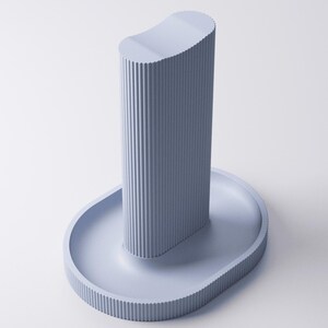 May include: A light periwinkle blue stand featuring a tall, vertical, ribbed cylindrical column with a concave top, mounted on an oval-shaped base with a matching ribbed edge. The entire object has a uniform matte finish and a structured design.