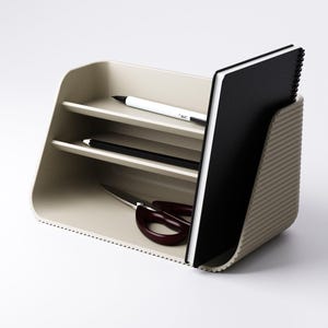 May include: A beige desk organizer with two shelves, holding a black notebook, a white pen, a black pencil, and burgundy scissors. The organizer has a ribbed side and a dotted edge, providing a stylish storage solution for office supplies.