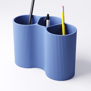 May include: A blue desk organizer with a wavy design, holding a black pen, a silver and black pen, and a yellow pencil. The organizer has a ribbed texture and is made of a solid, opaque material. The pencil has a pink eraser.