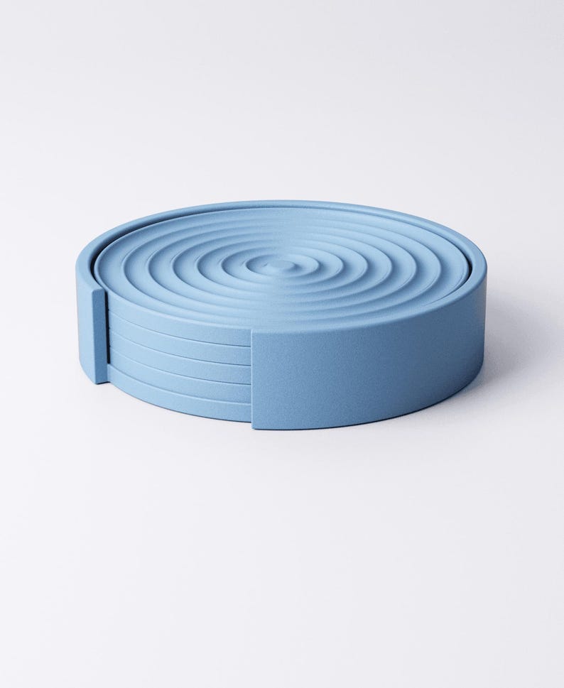 May include: A set of six light blue coasters, each with a ripple pattern on the top. The coasters are arranged in a circular stack, with a rectangular side piece for easy removal. The coasters are made of a solid material.