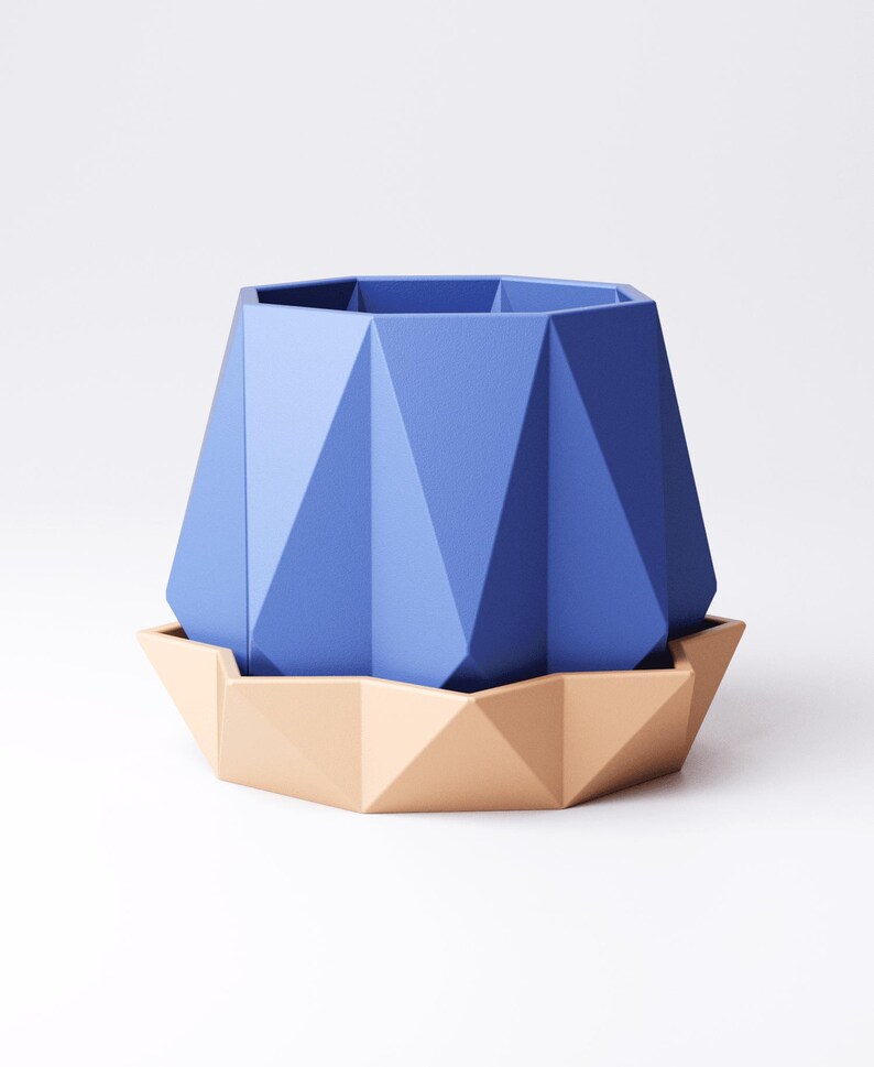 May include: A geometric blue planter with a matching beige saucer. The planter has a faceted design and a hexagonal top. The saucer is also faceted, creating a modern, minimalist aesthetic. The planter and saucer are made of a solid material.