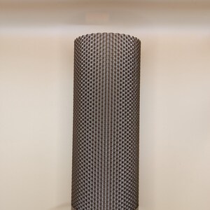 K&ouml;nnte beinhalten: Eine zylindrische Lampe mit einer strukturierten, dunkelbraunen Au&szlig;enseite. Die Lampe hat ein silbernes Band am Sockel, &uuml;ber einem hellblauen Abschnitt. Ein blaues Kabel erstreckt sich von der Basis. Die Lampe steht vor einer beigen Wand.