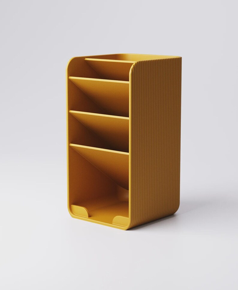 May include: Mustard yellow desk organizer with four angled compartments and a curved design. The organizer has a ribbed texture on the side and a small lip at the base. The product is designed to hold office supplies.