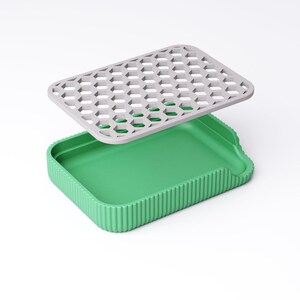 May include: A two-piece container set. The base is a bright green rectangular tray with vertical ridged sides. A gray, honeycomb-patterned lid hovers above the tray. The lid is rectangular with a series of hexagonal cutouts.