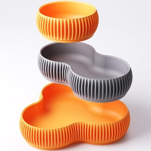 Pu&ograve; includere: Set di tre ciotole per animali domestici in arancione e grigio. Le ciotole hanno un design a coste e un'estetica moderna e minimalista. La ciotola superiore &egrave; rotonda, la ciotola centrale ha la forma di un otto e la ciotola inferiore ha la forma di un trifoglio.