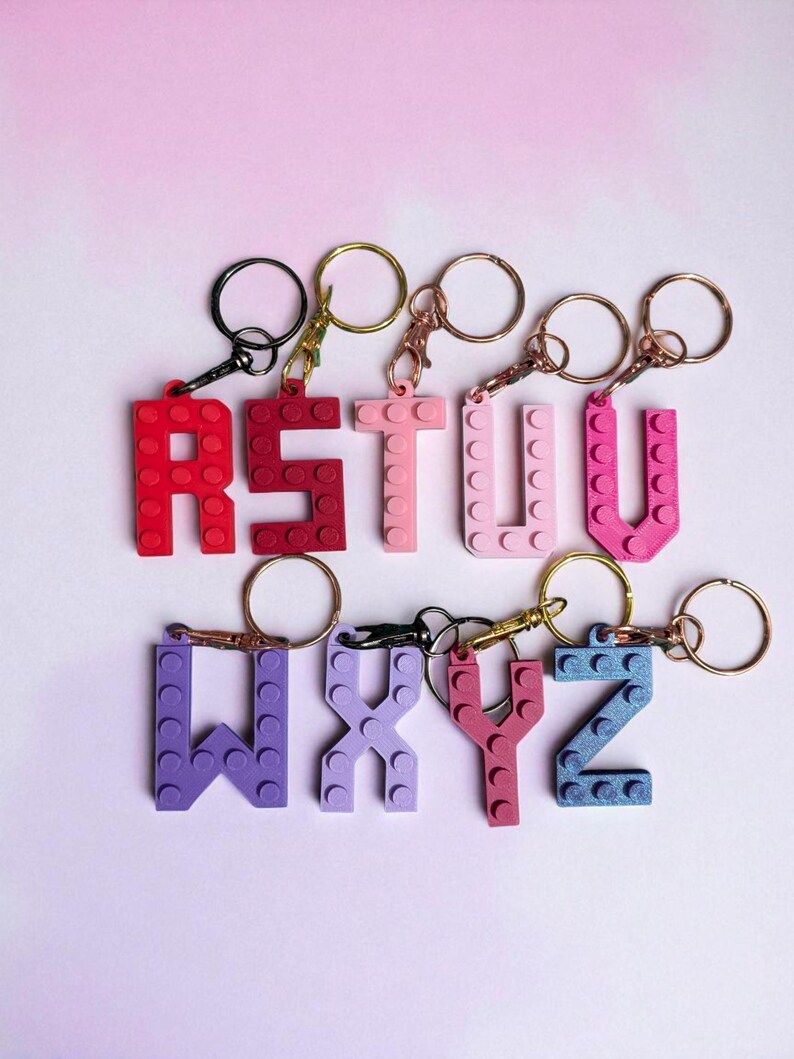 May include: A collection of colorful letter keychains, each crafted from interlocking brick-style pieces. The letters R, S, T, U, W, X, Y, and Z are displayed in shades of red, pink, purple, and blue, with gold and black key rings.