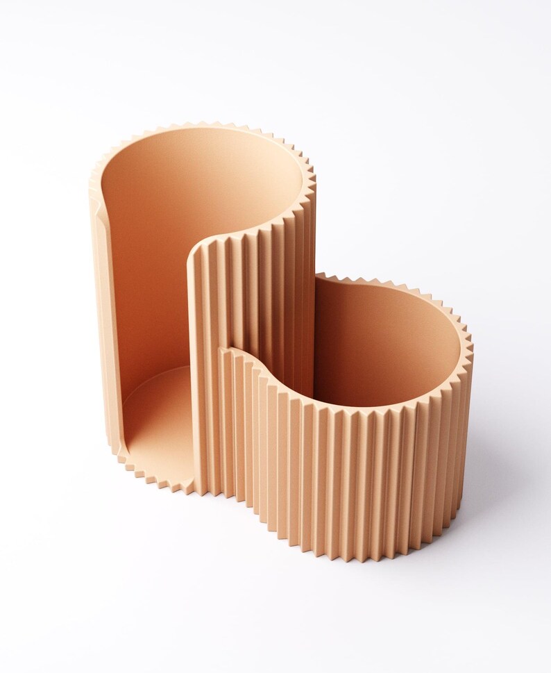 May include: A peach-colored, modern desk organizer with a unique, wavy design. The organizer features two open compartments of varying heights, each with vertical ridged detailing. The top edges have a sawtooth pattern. The minimalist design is suitable for office or home use.