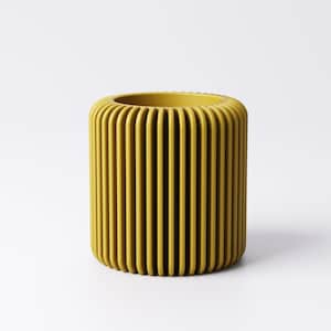 May include: A cylindrical, mustard-yellow container with vertical, rounded ridges. The top opening is also rounded. The container is set against a white background.