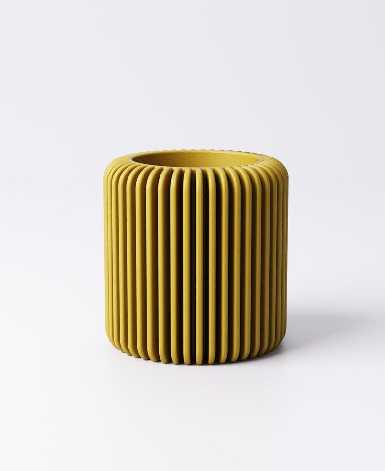 May include: A cylindrical, mustard-yellow container with vertical, rounded ridges. The top opening is also rounded. The container is set against a white background.