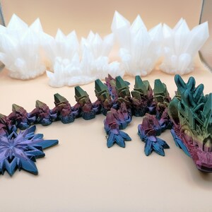 May include: A 3D-printed dragon with a multi-colored body and head, and a blue and purple star-shaped tail. Several white crystal formations are in the background. The dragon's head is detailed with various colors.