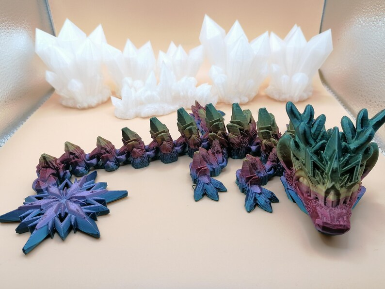 May include: A 3D-printed dragon with a multi-colored body and head, and a blue and purple star-shaped tail. Several white crystal formations are in the background. The dragon's head is detailed with various colors.