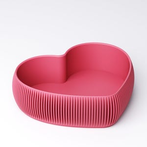 May include: A heart-shaped container in a vibrant pink hue. The container features a textured, ribbed exterior and a smooth interior. The design is modern and minimalist, suitable for various decorative or functional purposes.
