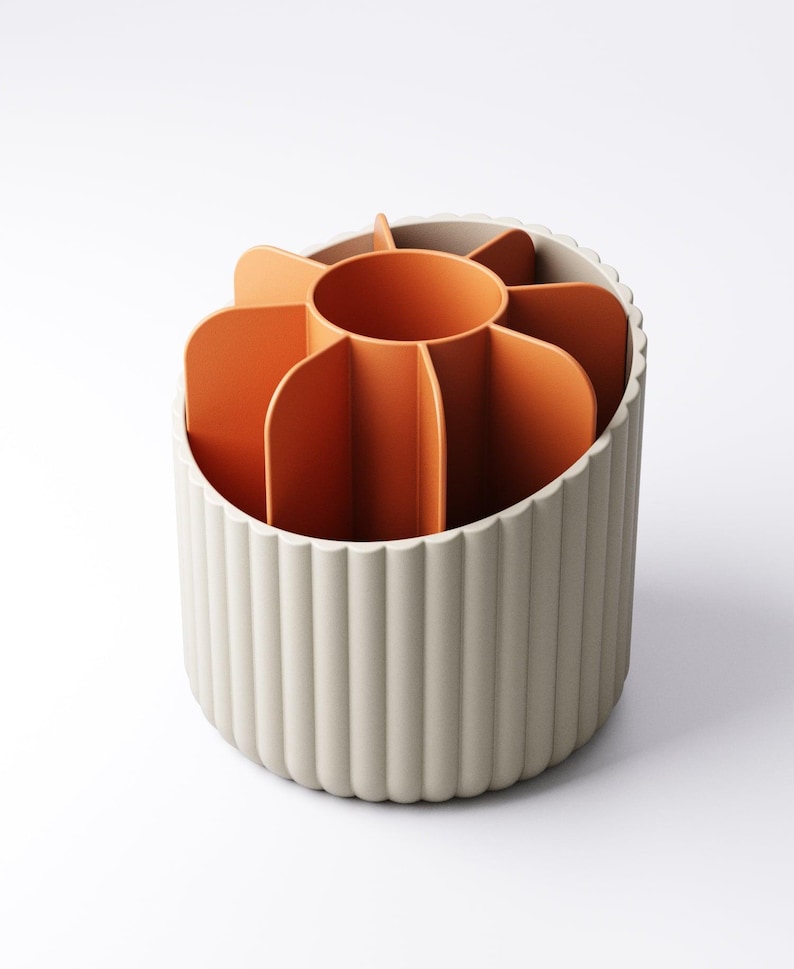 May include: A beige and orange desk organizer with a flower-like design. The organizer has a cylindrical base with vertical ridges and an interior divided into multiple sections. The interior is orange, and the exterior is beige.