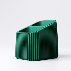 May include: A dark green desk organizer with a ribbed exterior. The organizer has two compartments and a slanted top. The vertical lines create a textured appearance. The product is made of a solid material and sits on a white surface.
