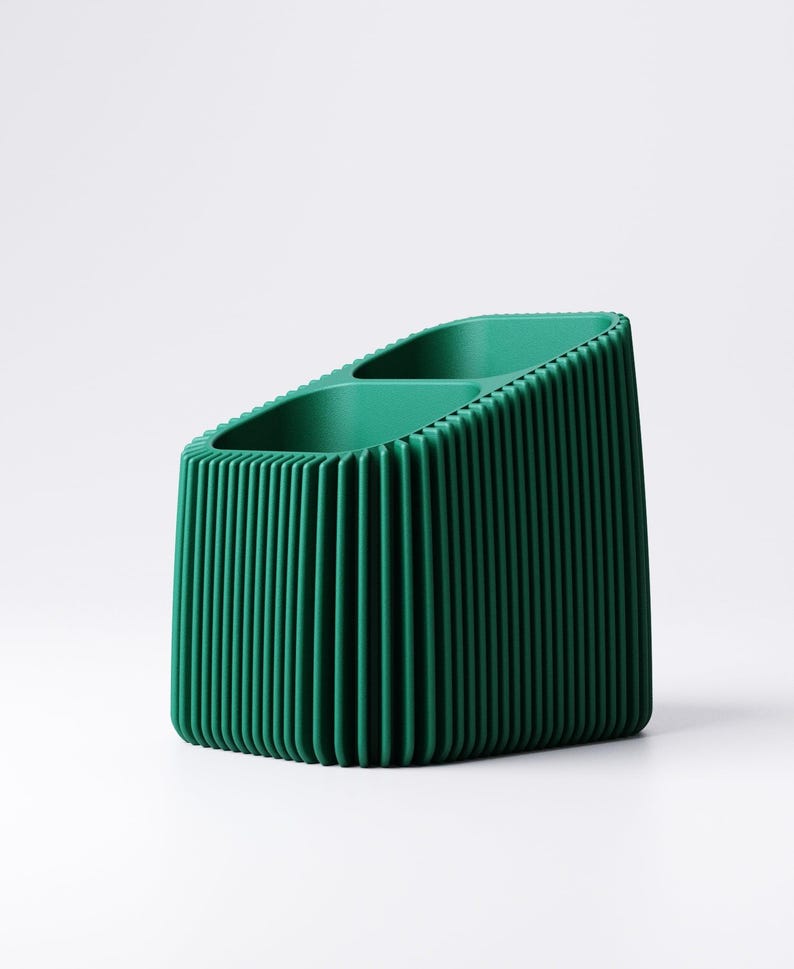 May include: A dark green desk organizer with a ribbed exterior. The organizer has two compartments and a slanted top. The vertical lines create a textured appearance. The product is made of a solid material and sits on a white surface.