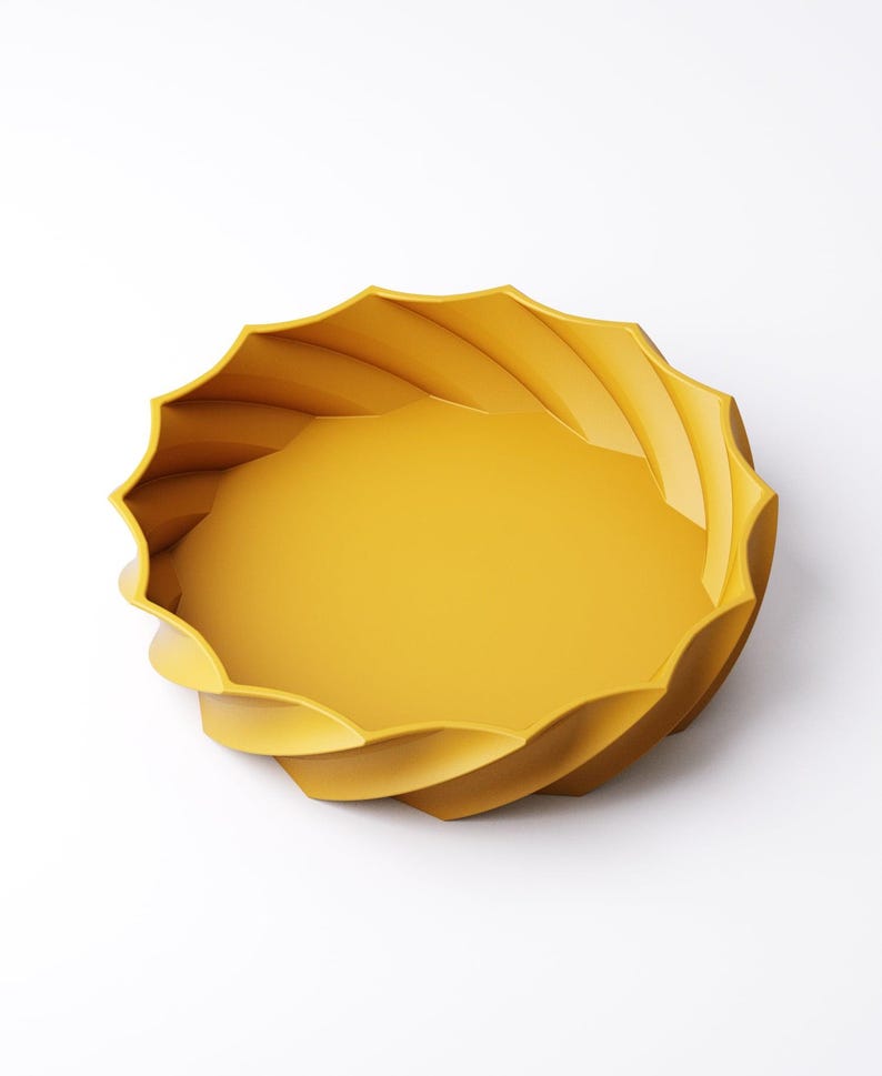 May include: A bright yellow decorative bowl with a unique, swirling design. The bowl has a round, shallow interior and a textured, wave-like exterior. The bowl is made of a solid material and is set against a white background.
