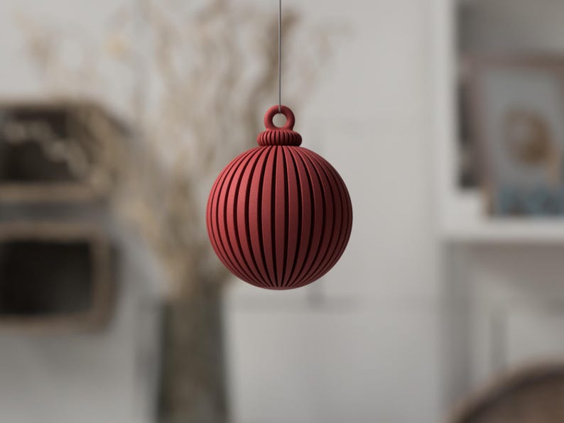 May include: A red, spherical ornament with vertical grooves and a loop for hanging. The decorative ball is suspended by a thin string, ideal for holiday or seasonal decor. The ornament's design features a ribbed texture.