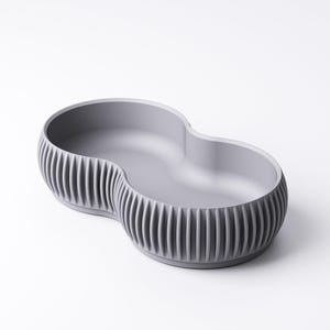 Pu&ograve; includere: Una ciotola in ceramica grigia a doppio lobo con esterno a coste. La ciotola ha un interno liscio e un design unico e moderno. Adatta per servire snack o come elemento decorativo.