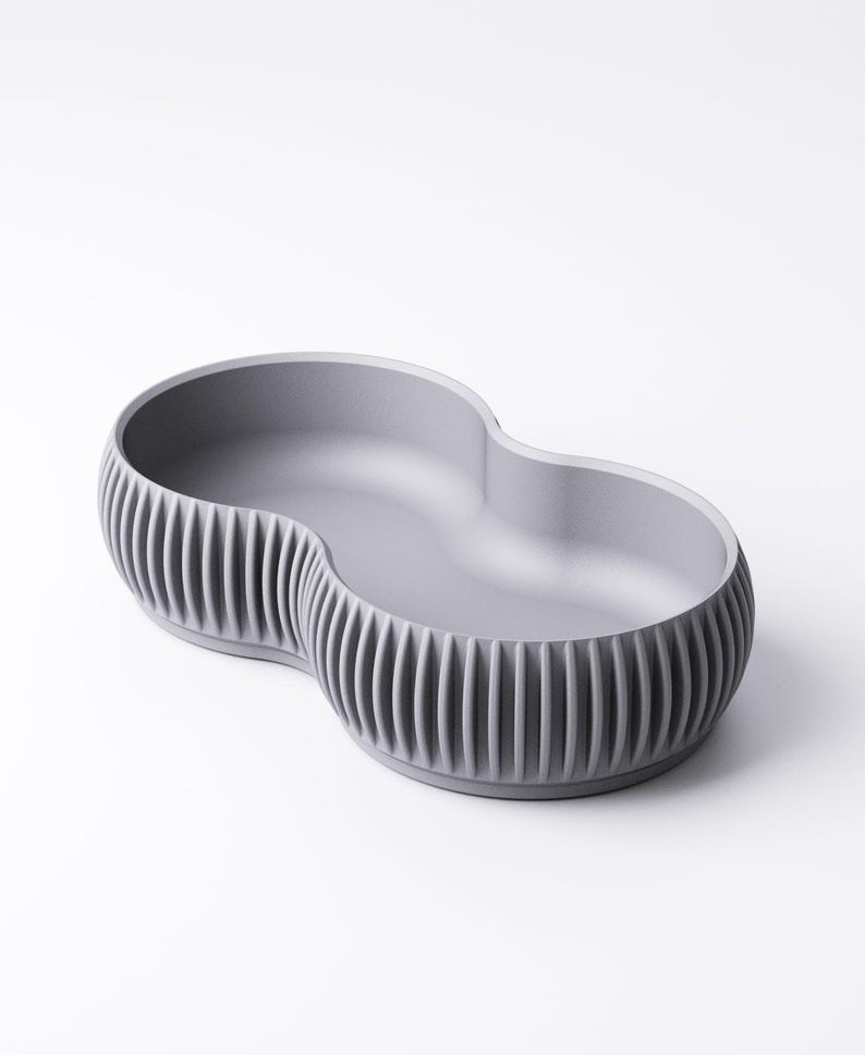 Pu&ograve; includere: Una ciotola in ceramica grigia a doppio lobo con esterno a coste. La ciotola ha un interno liscio e un design unico e moderno. Adatta per servire snack o come elemento decorativo.