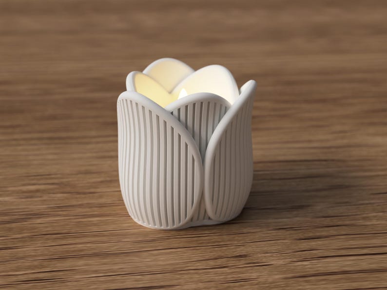 May include: A white, tulip-shaped candle holder with vertical ribbed detailing. The interior glows with a soft, warm light. The candle holder is made of a matte material and sits on a wooden surface. The design is modern and minimalist.