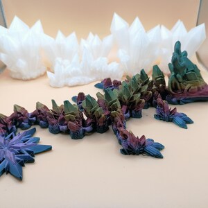 May include: A collection of 3D-printed crystal sculptures in various shapes and colors. The main piece is a multi-colored dragon-like figure with crystal formations. Additional white crystal clusters and a blue snowflake-shaped piece are also present.