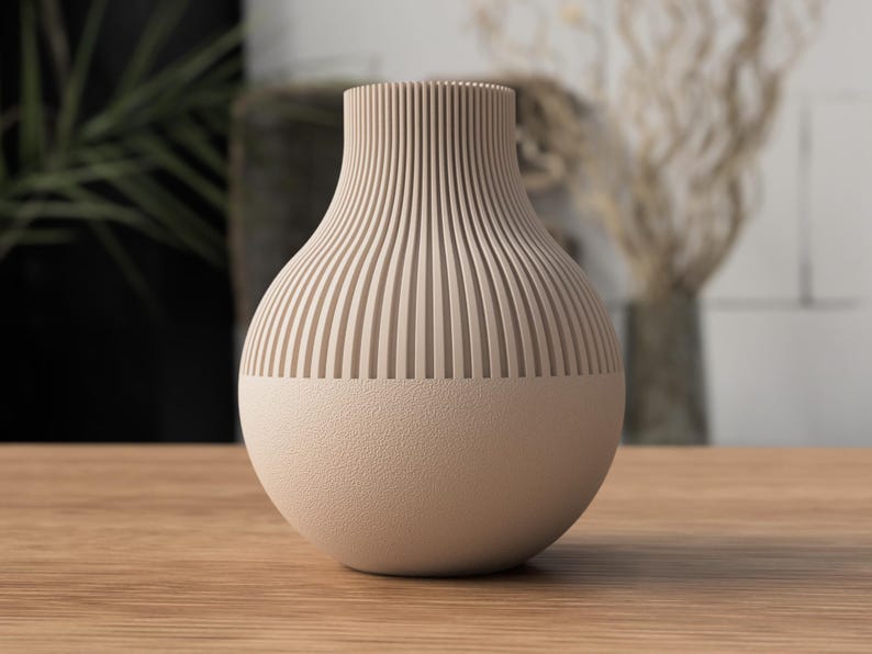 May include: A beige ceramic vase with a textured, ribbed upper section and a smooth, rounded base. The vase is displayed on a wooden surface, showcasing its neutral color and modern design. The vase is approximately 10 inches tall.