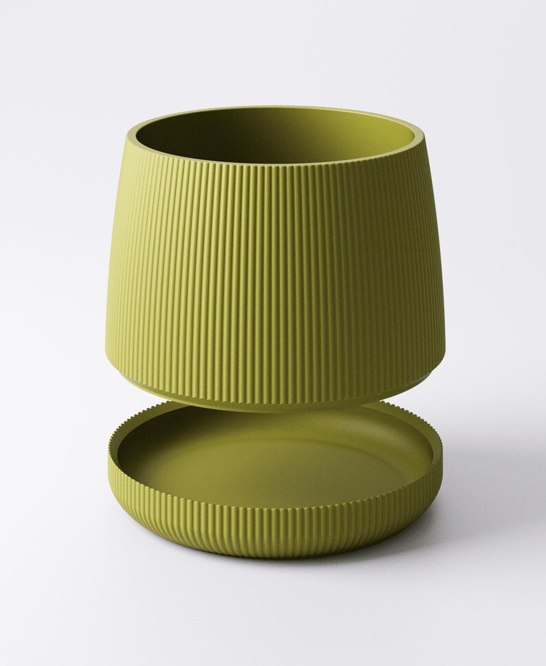 May include: A two-piece, olive-green planter with a ribbed texture. The upper section is a cylindrical pot, and the lower section is a matching saucer. The design is modern and minimalist, suitable for indoor or outdoor use.