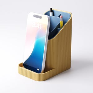 May include: A mustard yellow desk organizer with a blue interior. The organizer has a slot for a smartphone and compartments for pens and pencils. A white smartphone displays the time as 9:41. The organizer is made of a ribbed material.