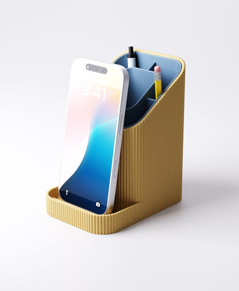 May include: A mustard yellow desk organizer with a blue interior. The organizer has a slot for a smartphone and compartments for pens and pencils. A white smartphone displays the time as 9:41. The organizer is made of a ribbed material.