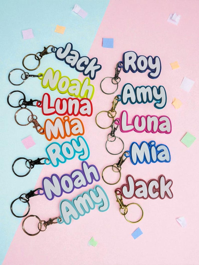 May include: A collection of colorful name keychains with various names like "Jack", "Noah", "Luna", "Mia", "Roy", and "Amy". Each keychain features a name in a bubble letter style with a contrasting outline and a metal clasp and ring.