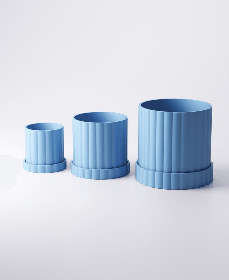 May include: Three light blue cylindrical planters of varying sizes, each with vertical ribbed detailing and a matching base. The planters are arranged from smallest to largest, showcasing a minimalist design.