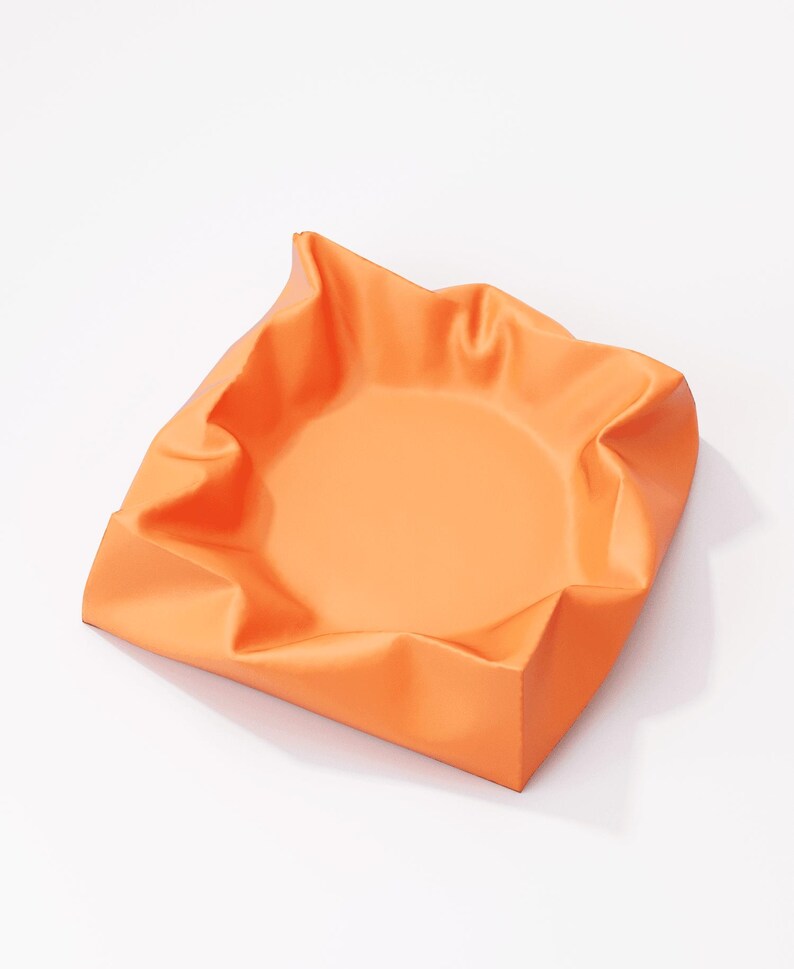 May include: An orange, square-shaped bowl with a slightly crumpled, folded rim. The bowl has a smooth, matte finish and sits on a white surface. The interior of the bowl is a lighter shade of orange.
