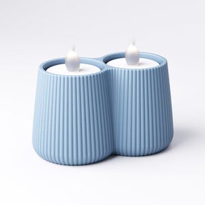May include: A light blue, double-candle holder with a ribbed design. The holder contains two white, battery-operated LED candles with a flickering flame effect. The candle holder is a decorative home accent.