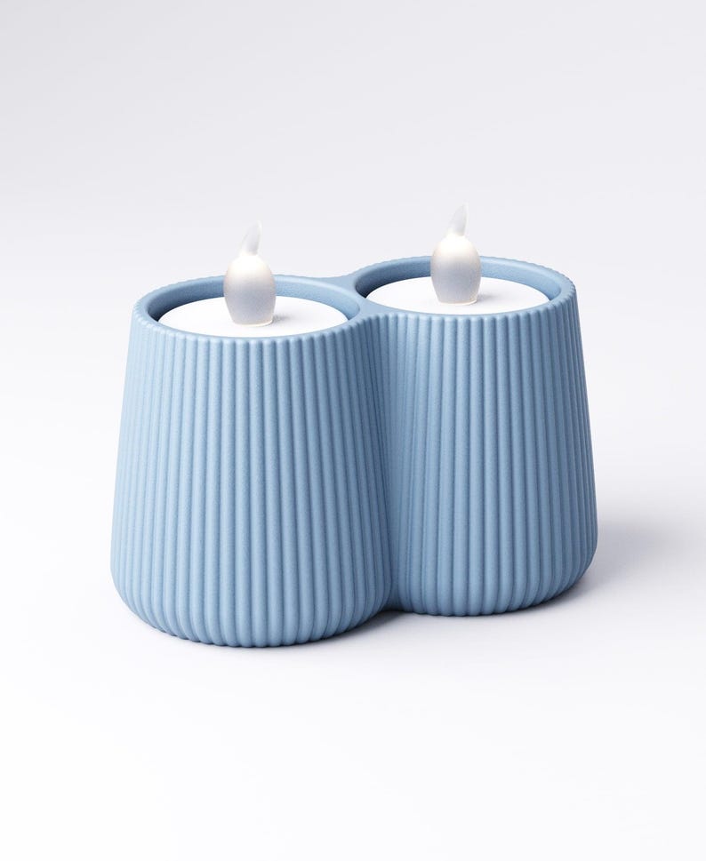 May include: A light blue, double-candle holder with a ribbed design. The holder contains two white, battery-operated LED candles with a flickering flame effect. The candle holder is a decorative home accent.