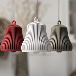May include: Three pendant lights in red, white, and olive green. Each bell-shaped light has vertical grooves and a loop at the top for hanging. The lights are suspended from thin cords against a blurred background.
