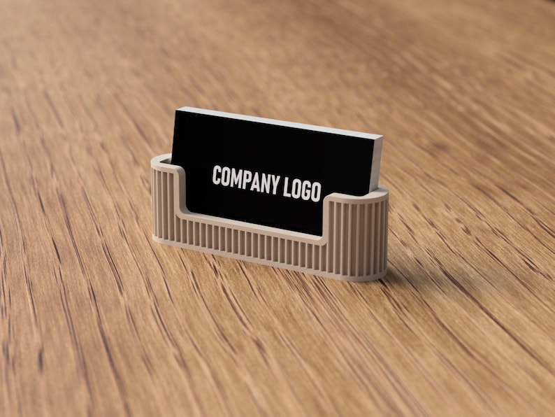 May include: A business card holder with a black card that reads "COMPANY LOGO" in white. The holder is a light beige color and has vertical lines. The background is a wooden surface.