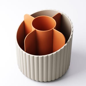 May include: A beige and orange desk organizer with a fluted exterior. The interior features an orange central cylinder and several orange dividers. The organizer is designed to hold pens, pencils, and other office supplies.
