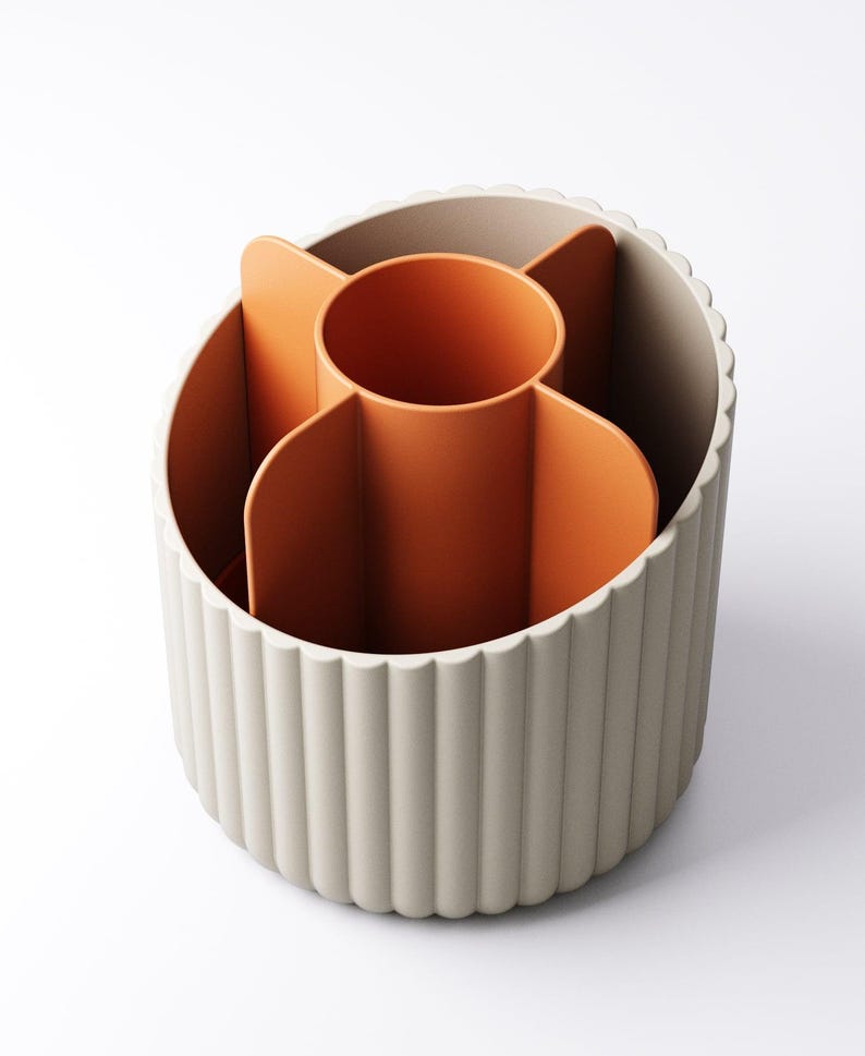 May include: A beige and orange desk organizer with a fluted exterior. The interior features an orange central cylinder and several orange dividers. The organizer is designed to hold pens, pencils, and other office supplies.