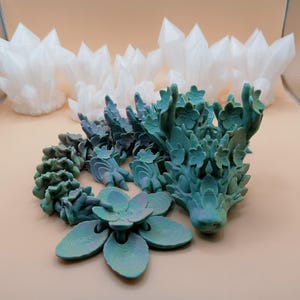 May include: A teal and green articulated dragon figurine with a flower and white crystal formations. The dragon has a detailed, textured design. The flower has six petals. The crystals are clustered together.