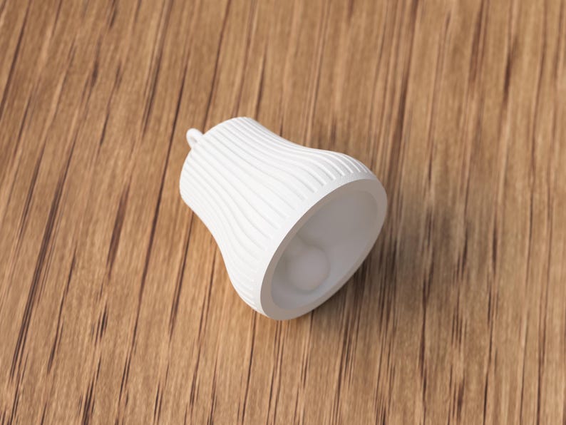 May include: A white, bell-shaped decorative object with a textured, ridged surface. The object has a small loop at the top and a smooth interior. The bell is resting on a wooden surface.