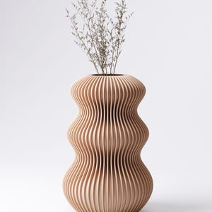 Peut inclure: Un vase moderne brun clair avec un design rainur&eacute; unique. Le vase a une forme bomb&eacute;e avec un col &eacute;troit et est rempli de tiges s&egrave;ches de couleur claire. Le vase est en bois et repose sur un fond blanc.