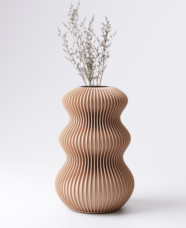 Peut inclure: Un vase moderne brun clair avec un design rainur&eacute; unique. Le vase a une forme bomb&eacute;e avec un col &eacute;troit et est rempli de tiges s&egrave;ches de couleur claire. Le vase est en bois et repose sur un fond blanc.