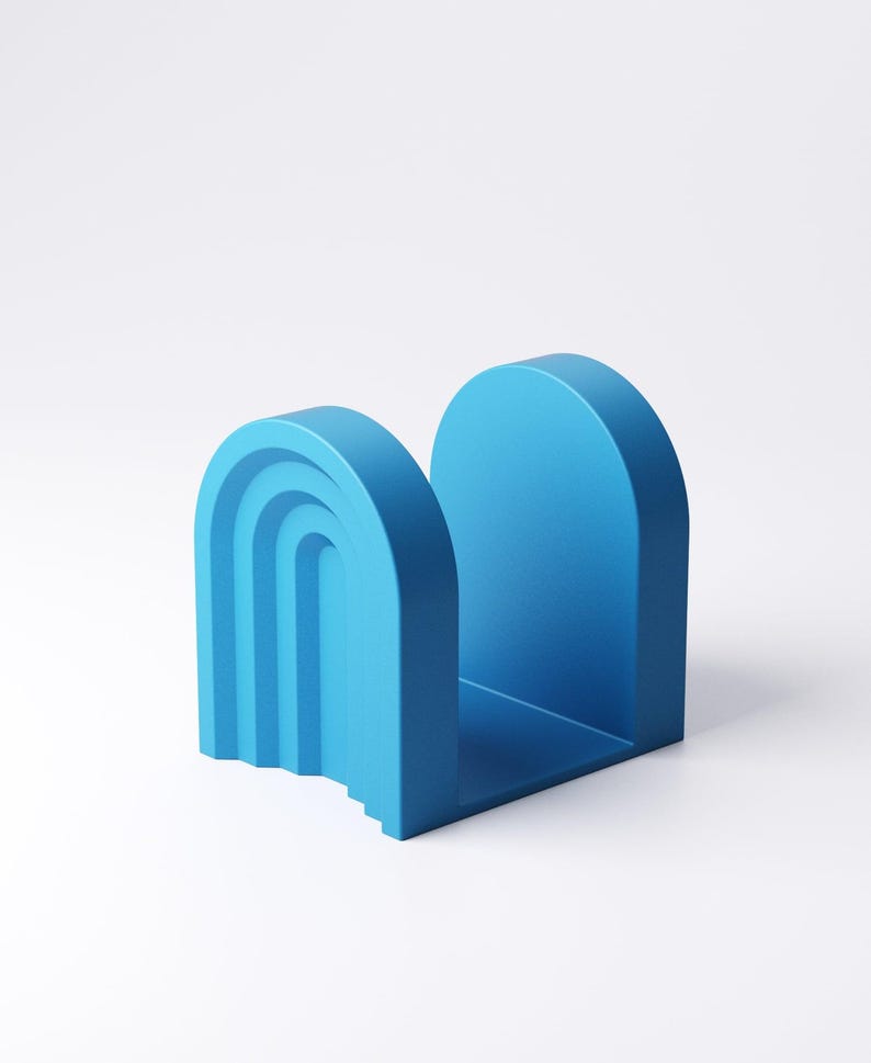 May include: A vibrant blue bookend with an arch design. One side features a layered, curved design, while the other is a solid arch. The bookend is made of a solid material and sits on a white surface.