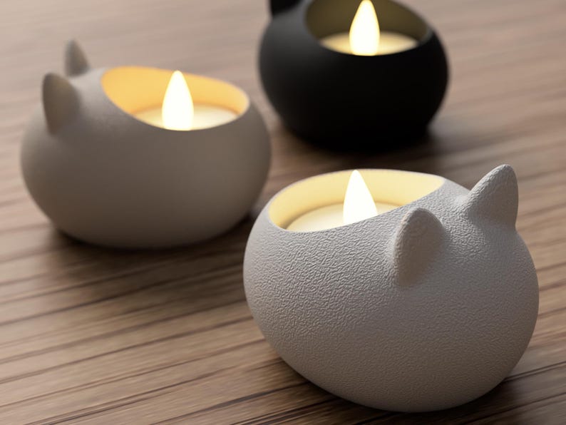 May include: Three cat-shaped candle holders in white and black, each with a lit, warm-toned LED candle. The holders are on a wooden surface, creating a cozy and decorative ambiance. The cat ear design adds a playful touch to the home decor.